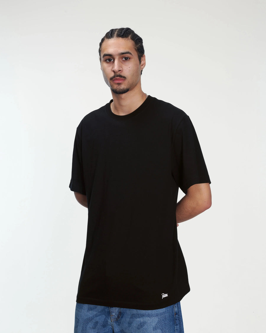 Model wearing a black Patta tubular cotton t-shirt with script logo above the hem.