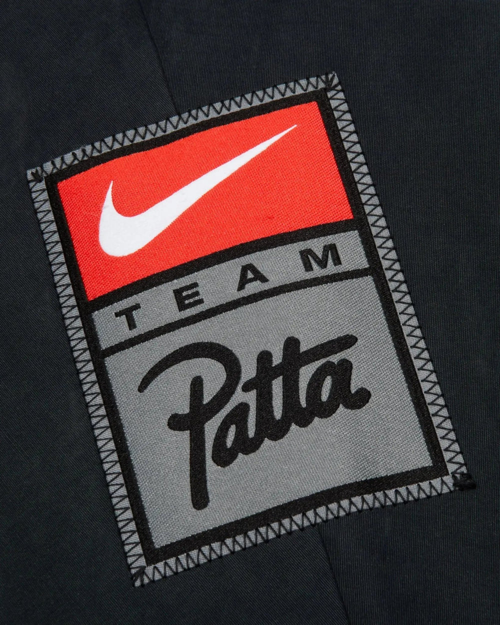 Detail of the embroidered Team Patta and Nike Swoosh patch on the black cotton track jacket.